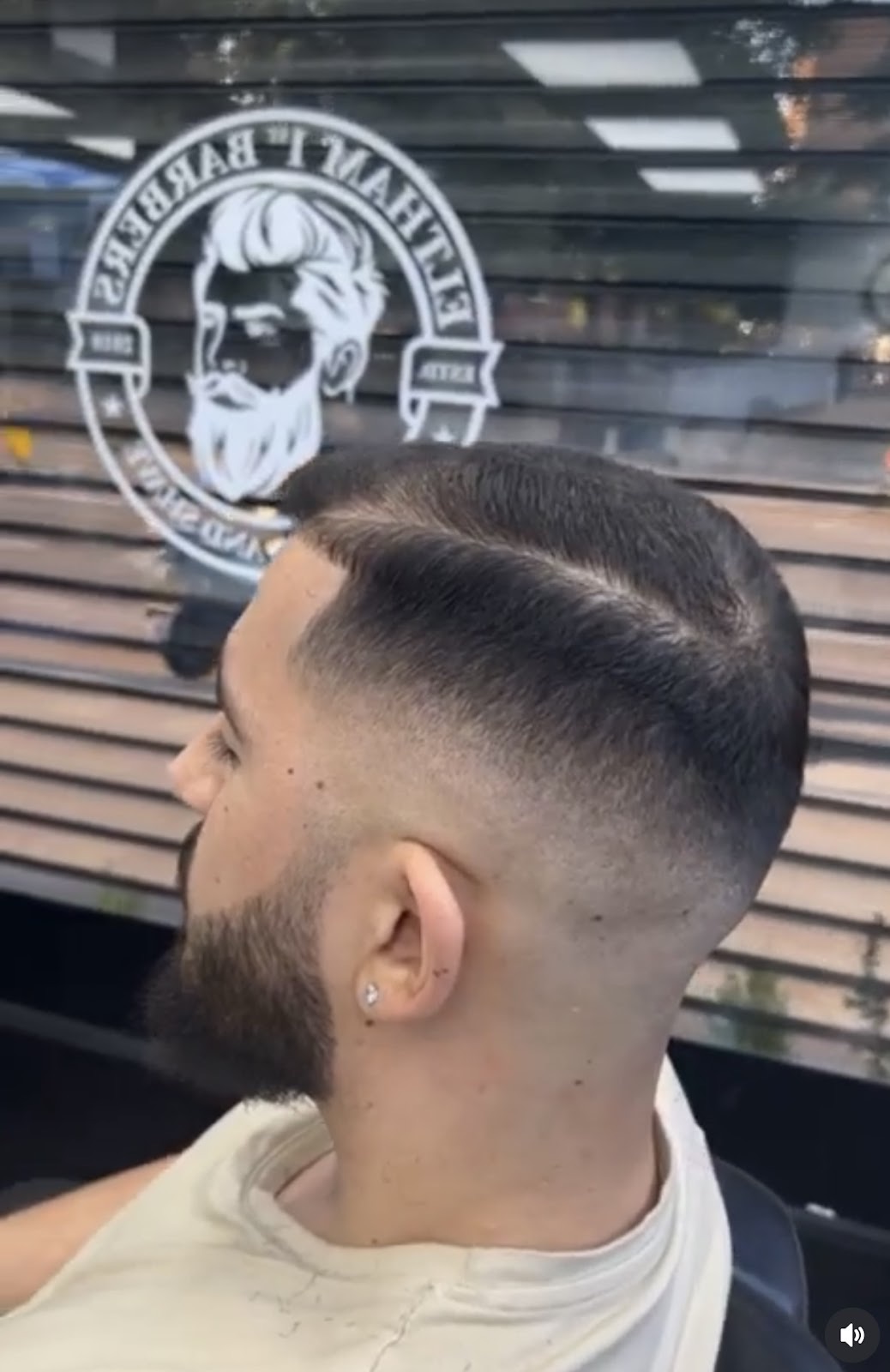 Side profile of a fresh skin fade and lined-up beard in the barber chair by the shop window